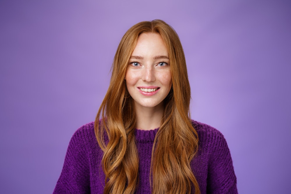 close up shot hopeful optimistic happy young redhead 20s girl with freckles long hair smiling joyfully with faith eyes prominent look posing against purple background Manitas a domicilio Madrid