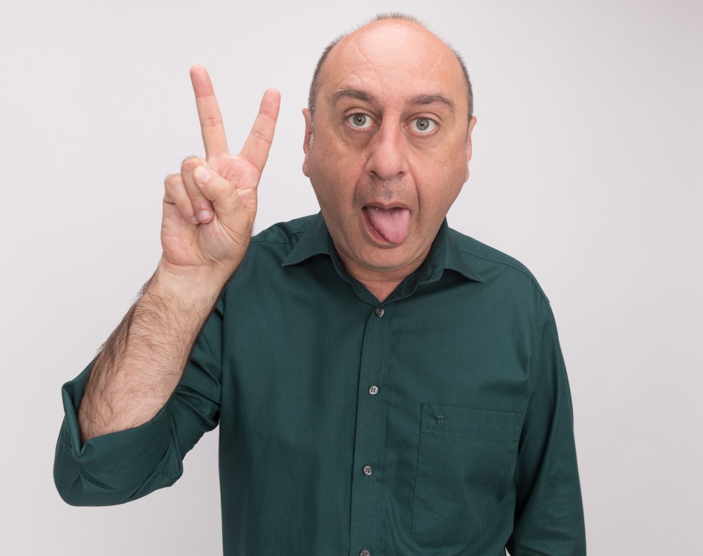 joyful-middle-aged-man-wearing-green-t-shirt-showing-tongue-doing-peace-gesture-isolated-white-wall