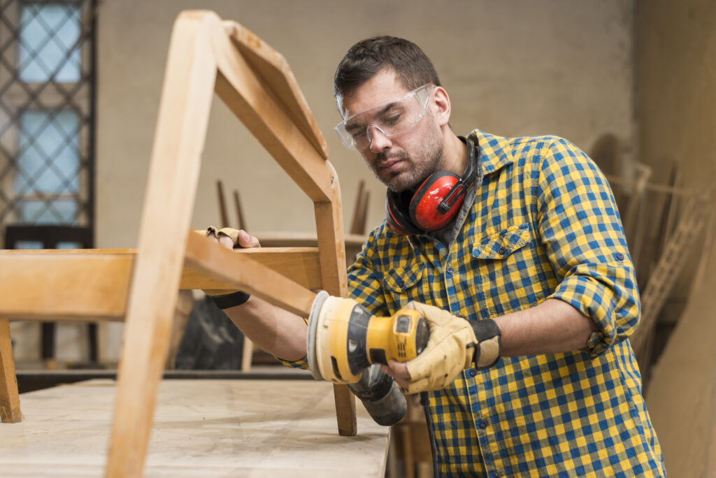 male carpenter wearing safety glasses using sander furniture workshop Carpintero